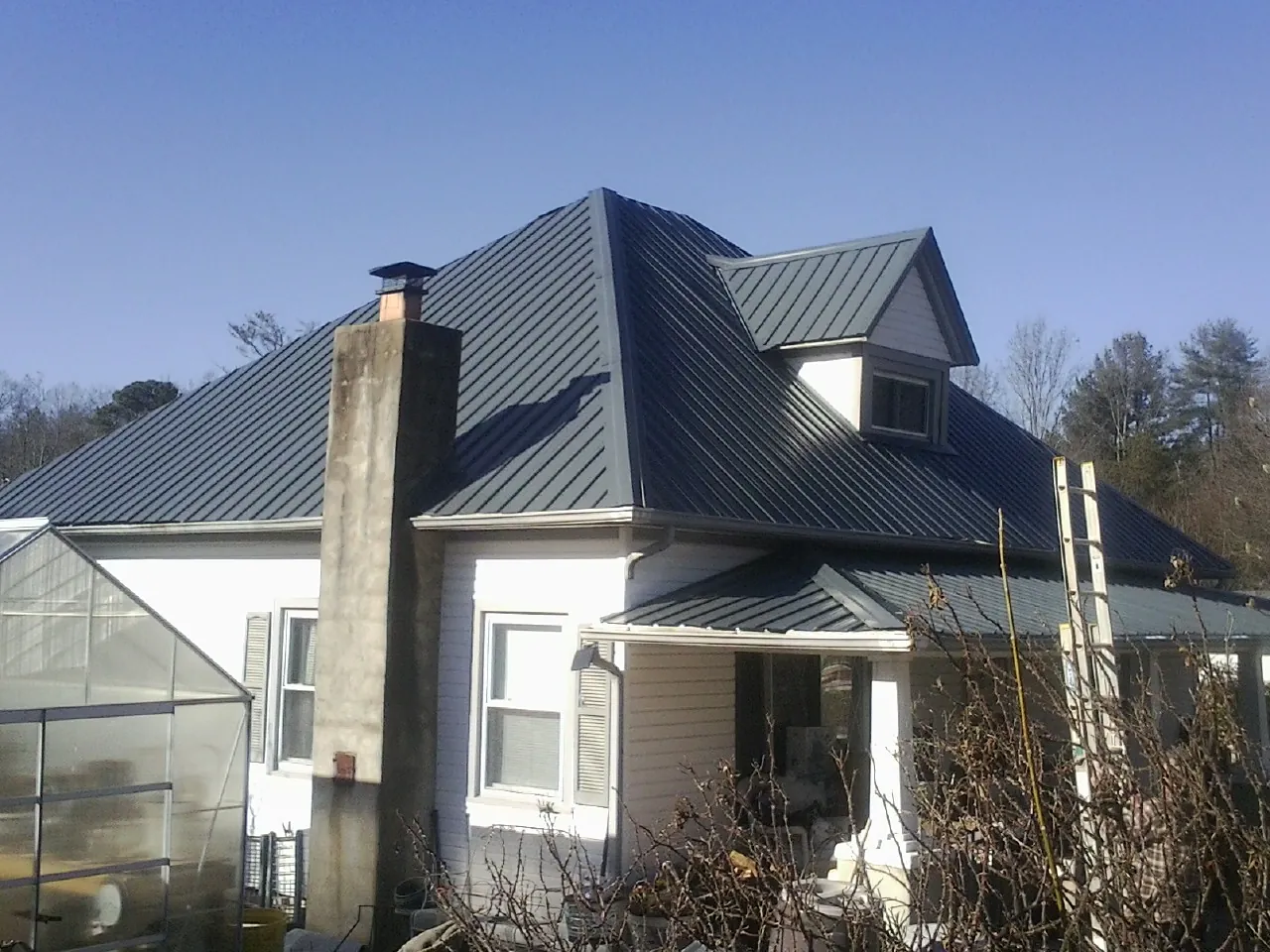 Dark blue standing seam metal roof on a white farmhouse with dormer — Slate & Tile Roof Repair by Roofing Brothers in Pickens