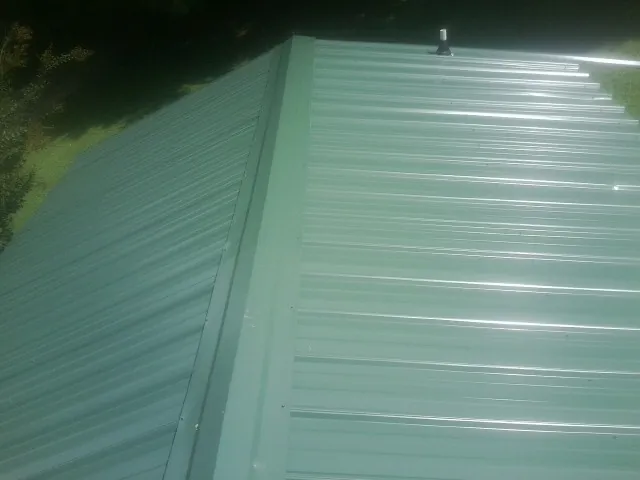 New green metal panels meeting at the ridge of a roof — Flat Roof Repair work by our crew in Pickens