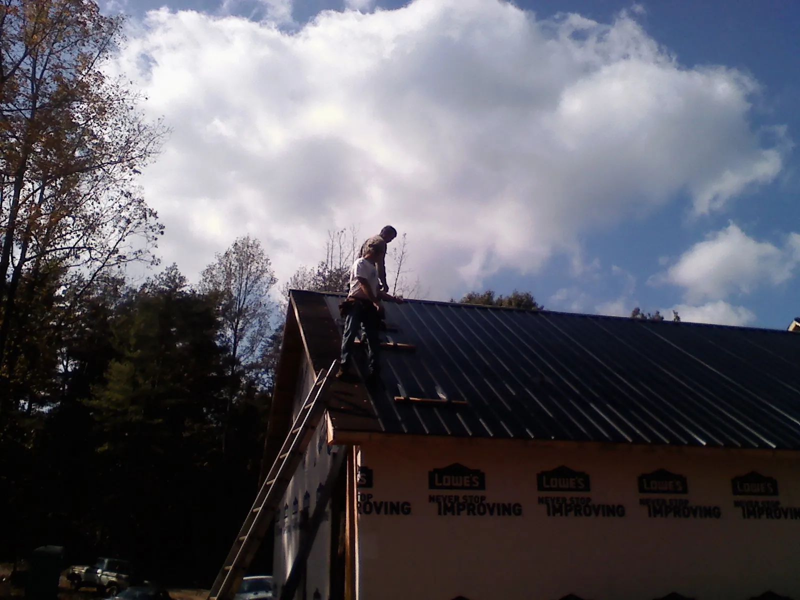 Roofer fastening dark metal panels high against a cloudy sky, from a Roof Inspection job in Pickens