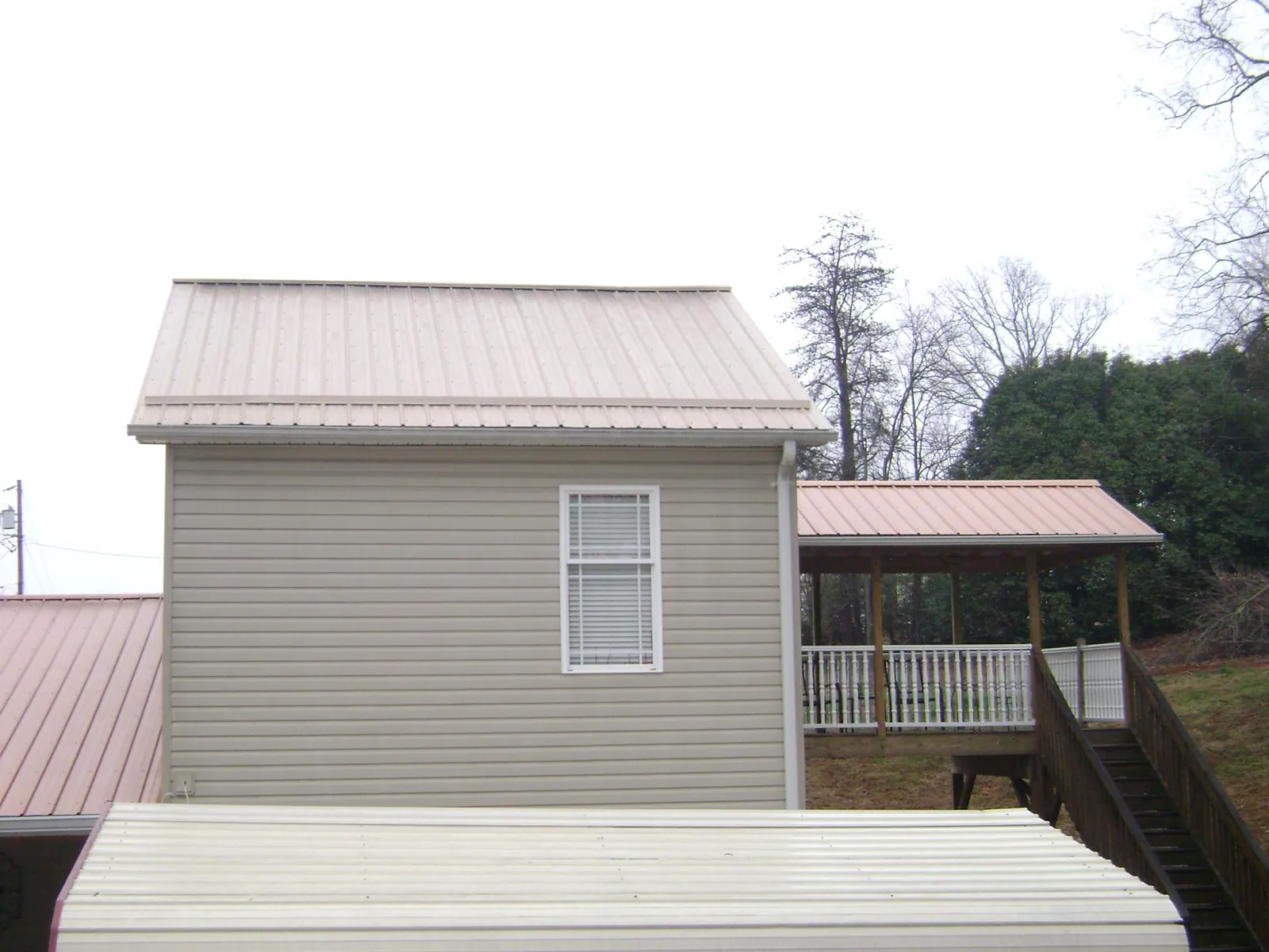 Tan metal roofs on a two story addition and attached porch, from a Roof Replacement job in Pickens